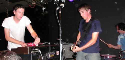 The guitarist and keyboardist from The Constantines, with their drummer in the background, while they totally rock out