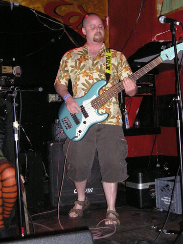 The bassist for a goth rock band wears a Hawaiian shirt
